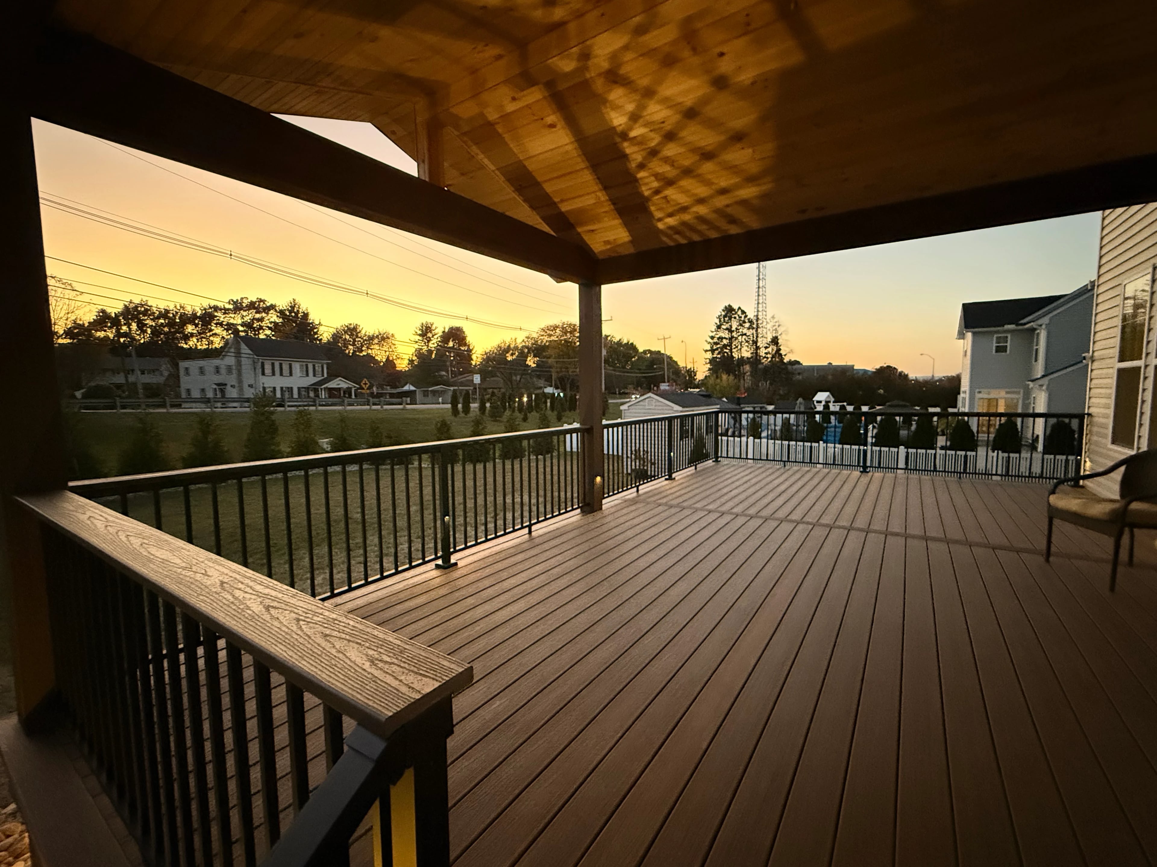 Inside a VM Power covered deck, showing the timber ceiling, composite decking, and black railing at sunset